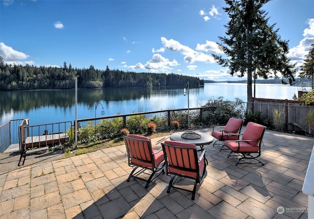 view of patio with a fenced backyard, a view of trees, a water view, and a fire pit