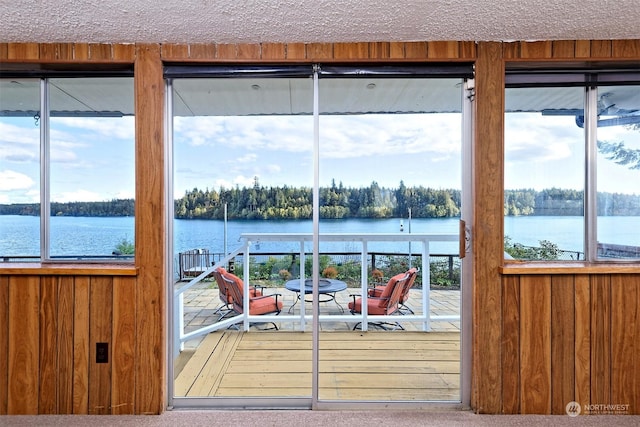 doorway to outside featuring a water view, a textured ceiling, and wood walls