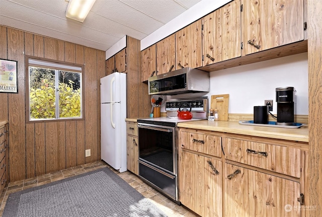 kitchen with freestanding refrigerator, wood walls, range with electric stovetop, light countertops, and stainless steel microwave