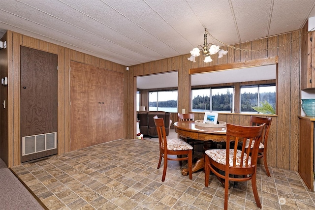 dining room with wooden walls, a notable chandelier, and visible vents