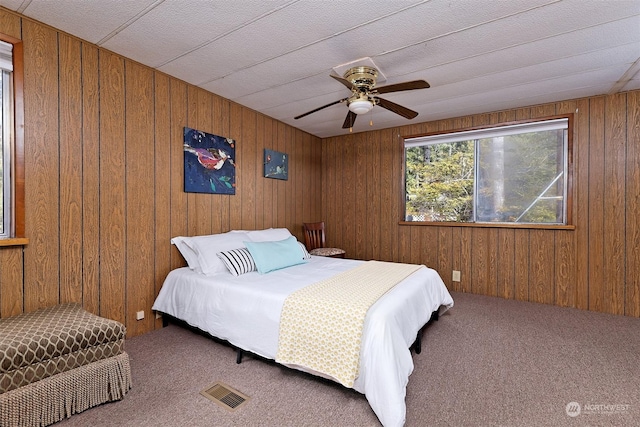 carpeted bedroom featuring wooden walls, a ceiling fan, and visible vents