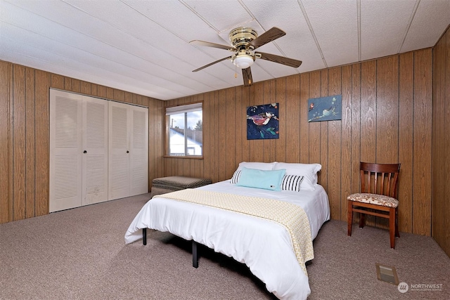 carpeted bedroom with ceiling fan, wood walls, and a closet