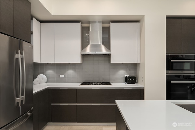 kitchen with appliances with stainless steel finishes, wall chimney exhaust hood, white cabinets, and tasteful backsplash