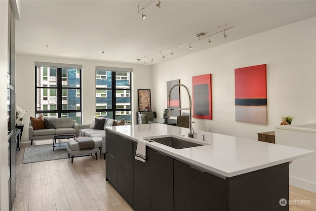 kitchen with sink, a kitchen island with sink, rail lighting, and light wood-type flooring