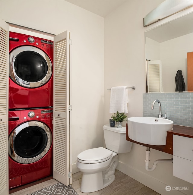 bathroom featuring decorative backsplash, toilet, stacked washing maching and dryer, hardwood / wood-style floors, and sink