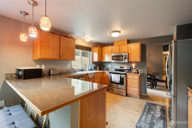 kitchen with a breakfast bar area, kitchen peninsula, stainless steel appliances, sink, and decorative light fixtures