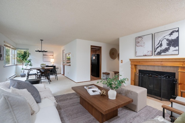 living room with light carpet, a notable chandelier, a textured ceiling, a fireplace, and a baseboard radiator