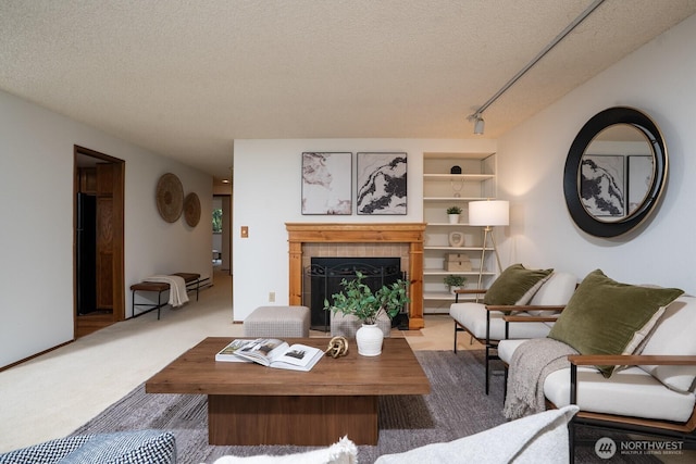 carpeted living area featuring a tiled fireplace, built in features, rail lighting, and a textured ceiling