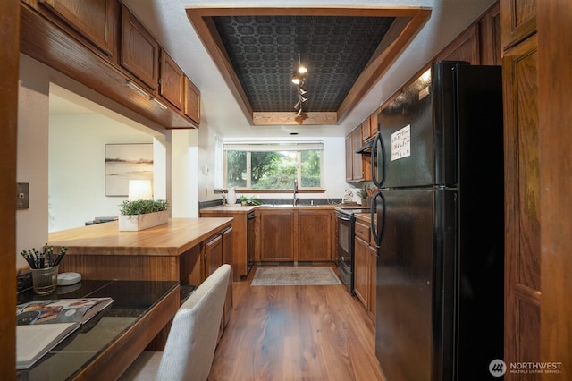 kitchen with black appliances, light wood-style floors, brown cabinets, and a tray ceiling