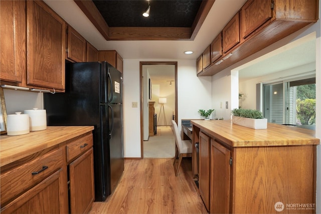 kitchen featuring a tray ceiling, light wood finished floors, brown cabinets, and wooden counters