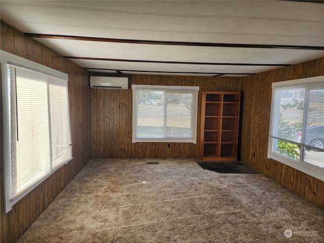 carpeted spare room featuring a wall mounted air conditioner, beam ceiling, wooden walls, and a wealth of natural light