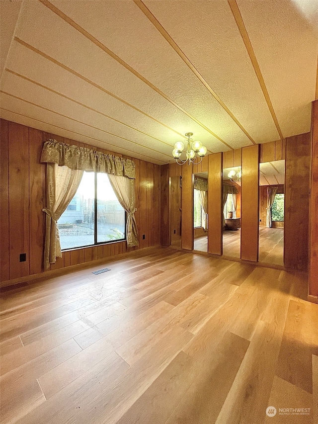 spare room with a chandelier, wood-type flooring, and wood walls