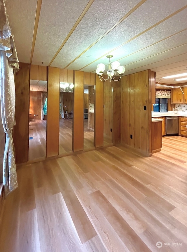 interior space with light hardwood / wood-style floors, a notable chandelier, a textured ceiling, and wooden walls