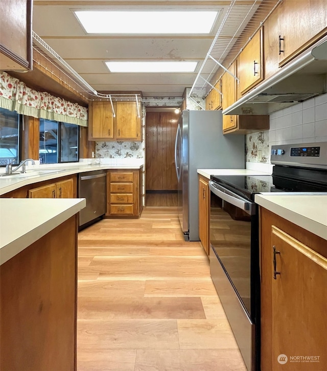 kitchen with stainless steel appliances, tasteful backsplash, sink, and light wood-type flooring