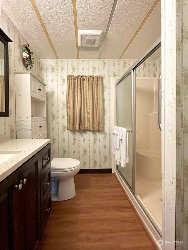 bathroom featuring a textured ceiling, a shower with shower door, toilet, vanity, and hardwood / wood-style flooring