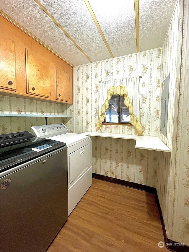 clothes washing area with light hardwood / wood-style flooring, a textured ceiling, electric panel, and washing machine and clothes dryer