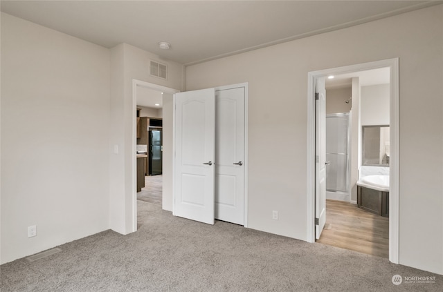 unfurnished bedroom featuring black refrigerator, light carpet, and ensuite bath