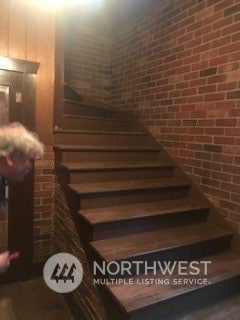 stairs with brick wall and hardwood / wood-style floors