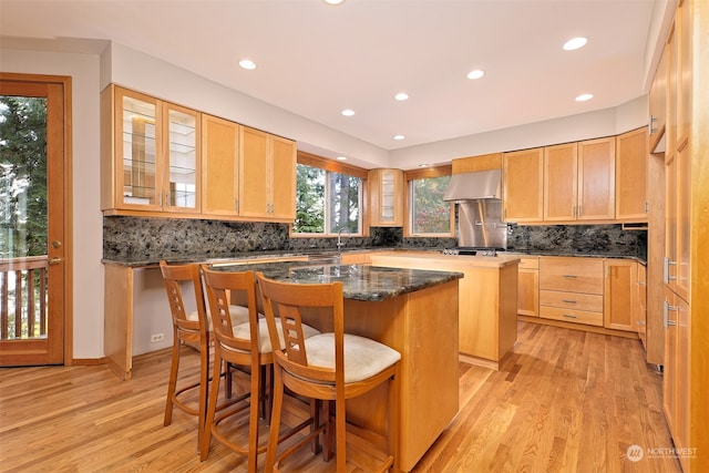 kitchen featuring a center island, a kitchen breakfast bar, ventilation hood, decorative backsplash, and light wood-type flooring