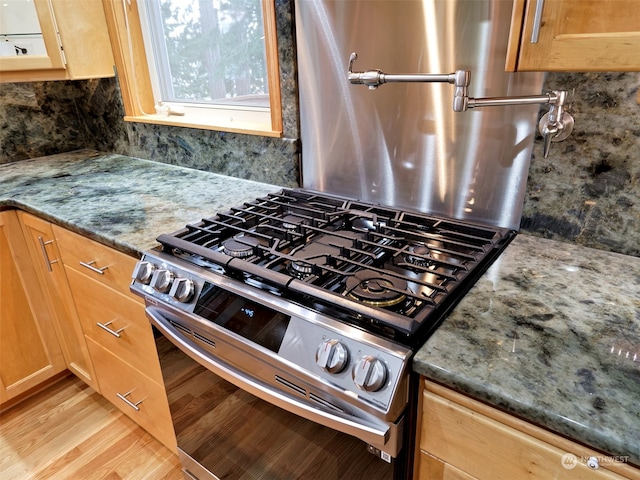 details with tasteful backsplash, light hardwood / wood-style flooring, dark stone counters, and stainless steel range with gas stovetop