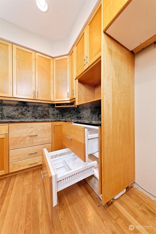 kitchen featuring light hardwood / wood-style flooring, dark stone countertops, and backsplash