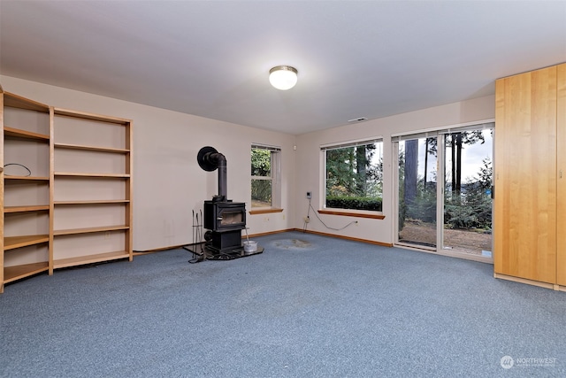 unfurnished living room featuring carpet floors, a wood stove, and a healthy amount of sunlight