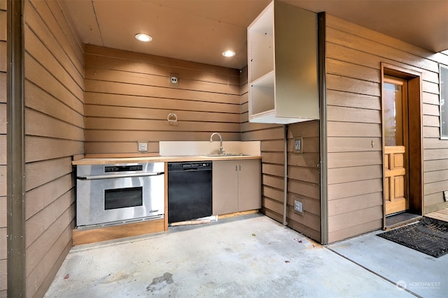 kitchen featuring wood walls, stainless steel oven, dishwasher, and sink