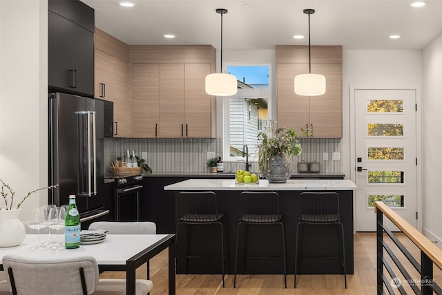 kitchen featuring a breakfast bar area, backsplash, high quality fridge, light brown cabinetry, and decorative light fixtures