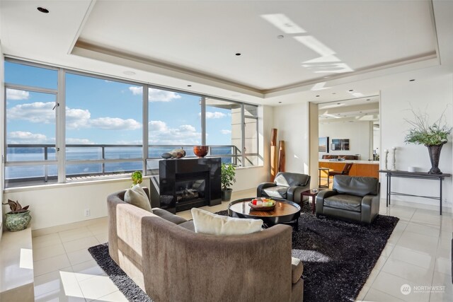 tiled living room featuring a wealth of natural light, a water view, and a tray ceiling