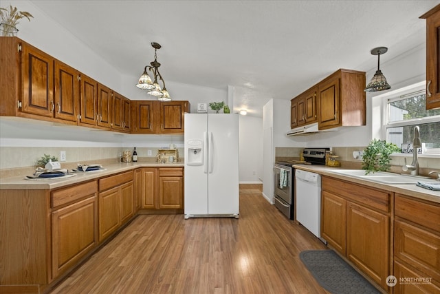 kitchen with white appliances, sink, hanging light fixtures, vaulted ceiling, and light hardwood / wood-style floors