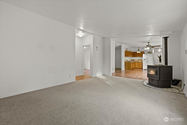 unfurnished living room with a wood stove, ceiling fan, and light hardwood / wood-style flooring