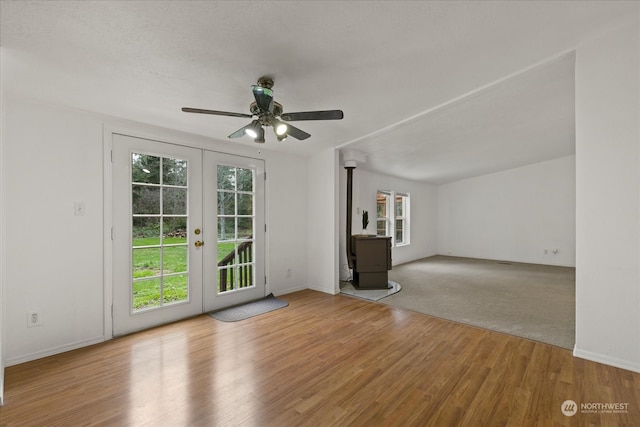 unfurnished living room featuring a wood stove, ceiling fan, french doors, and light wood-type flooring