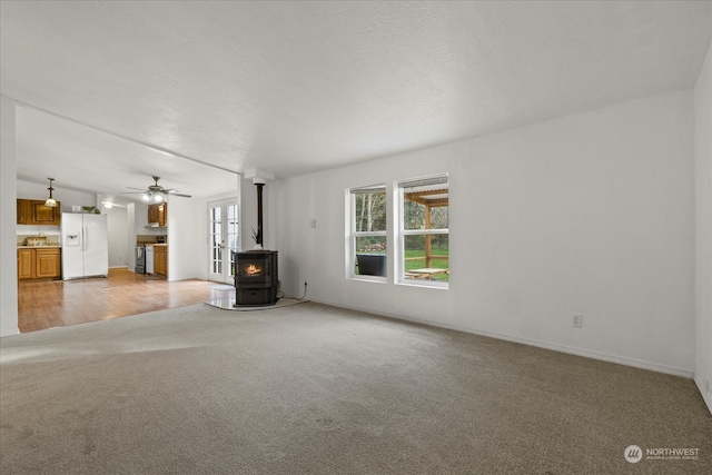 unfurnished living room featuring a textured ceiling, light hardwood / wood-style flooring, a wood stove, and ceiling fan