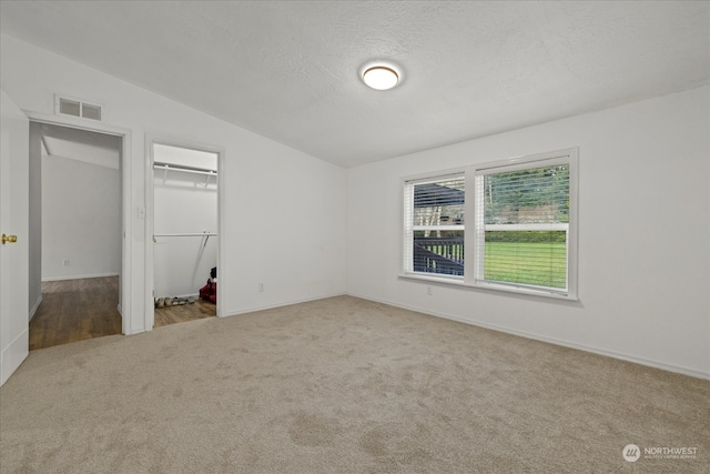 unfurnished bedroom featuring a spacious closet, light colored carpet, a textured ceiling, lofted ceiling, and a closet