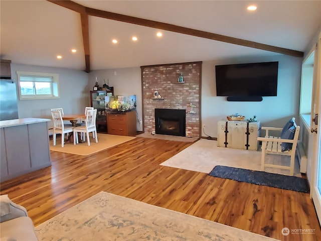 living room with light hardwood / wood-style floors, lofted ceiling with beams, and a brick fireplace