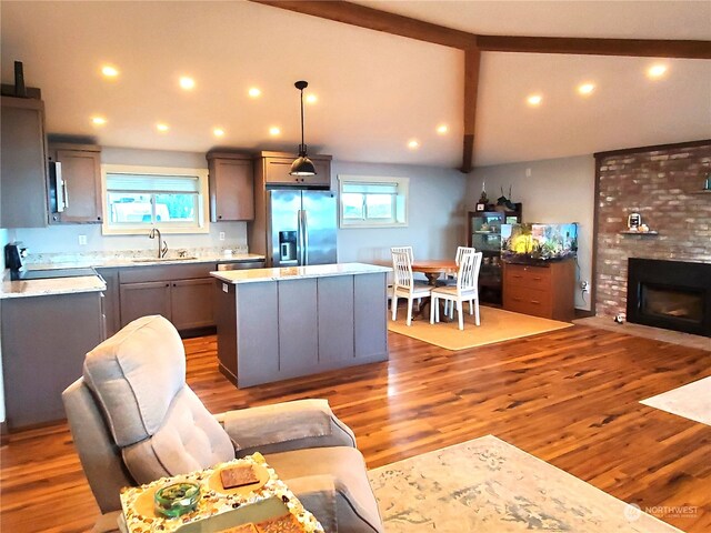 kitchen with a kitchen island, stainless steel refrigerator with ice dispenser, wood-type flooring, sink, and decorative light fixtures