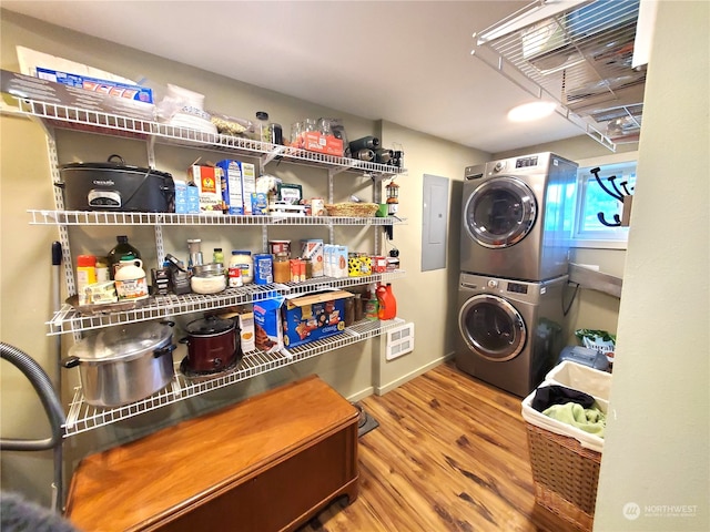 clothes washing area with electric panel, stacked washer and dryer, and wood-type flooring