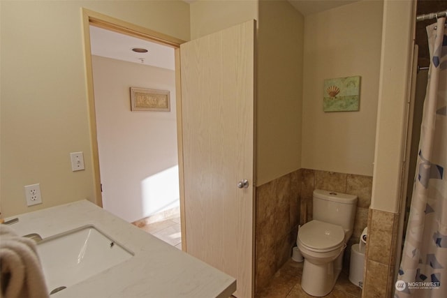 bathroom with tile patterned flooring, toilet, a sink, tile walls, and wainscoting