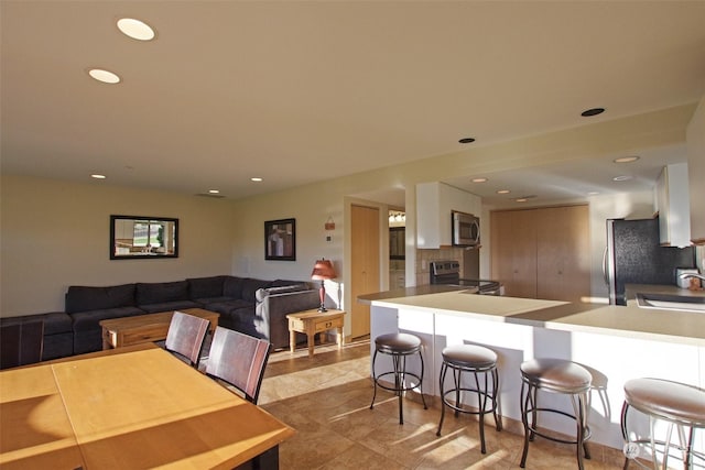 kitchen featuring stainless steel appliances, a sink, tasteful backsplash, a breakfast bar area, and white cabinetry