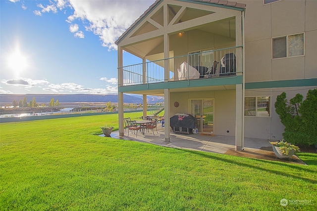 rear view of house featuring a water view, a patio, a lawn, and a balcony