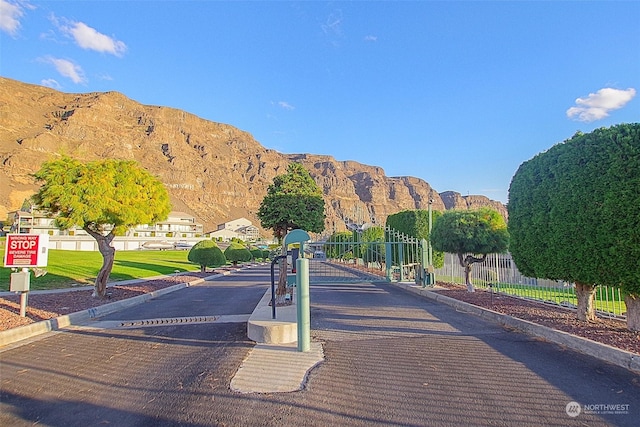 view of road featuring a gated entry, curbs, traffic signs, and a mountain view