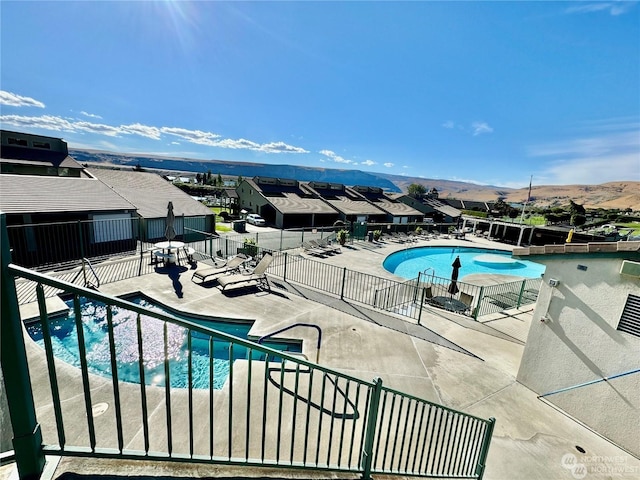 community pool featuring a residential view, a mountain view, central AC, fence, and a patio area