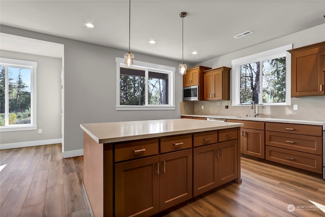 kitchen featuring a kitchen island, stainless steel microwave, wood-type flooring, decorative light fixtures, and tasteful backsplash