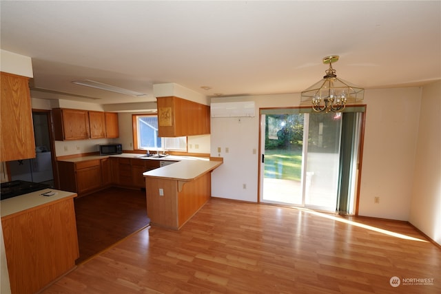 kitchen featuring a wall unit AC, kitchen peninsula, a notable chandelier, decorative light fixtures, and light wood-type flooring