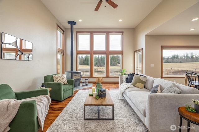 living room featuring baseboards, dark wood finished floors, a ceiling fan, a wood stove, and recessed lighting