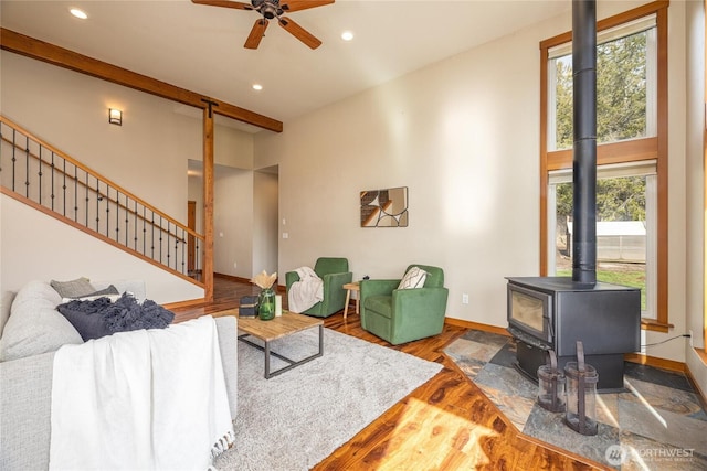 living room featuring stairs, a towering ceiling, wood finished floors, and a wood stove