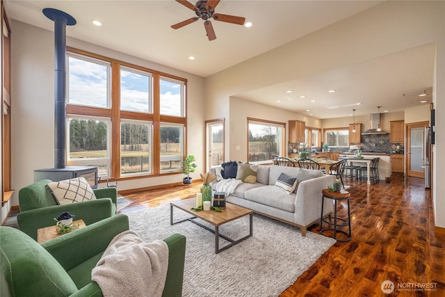 living room with baseboards, a ceiling fan, dark wood-type flooring, a wood stove, and recessed lighting