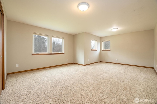 spare room featuring light colored carpet and baseboards