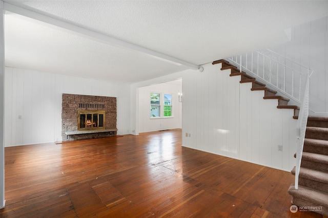 unfurnished living room with a stone fireplace, a textured ceiling, hardwood / wood-style floors, beamed ceiling, and wooden walls