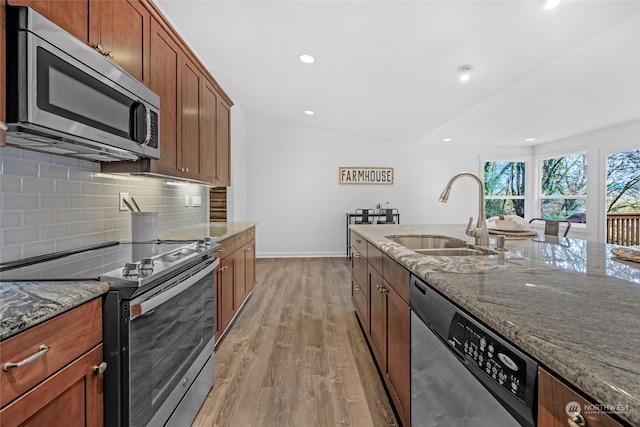 kitchen featuring lofted ceiling, stone countertops, stainless steel appliances, sink, and light hardwood / wood-style floors